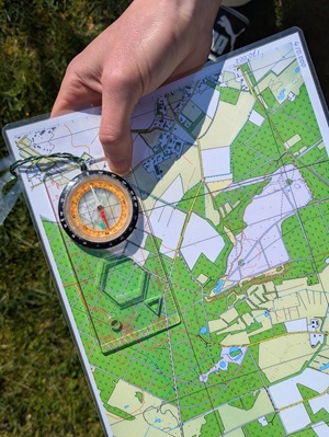 Hand houdt een kaart vast met een kompas er bovenop, klaar voor navigatie in het groen.