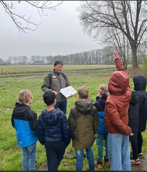 Buitenles over natuur: een gids met dierenfoto's in het veld omringd door kinderen.
