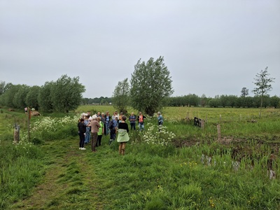 Groep mensen verzameld in een groen landschap onder bewolkte lucht.
