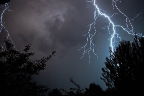 Bliksemflitsen in de nachtelijke lucht boven silhouet van bomen.