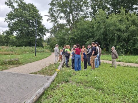 Een groep mensen staat in een groene parkachtige omgeving met bomen op de achtergrond.