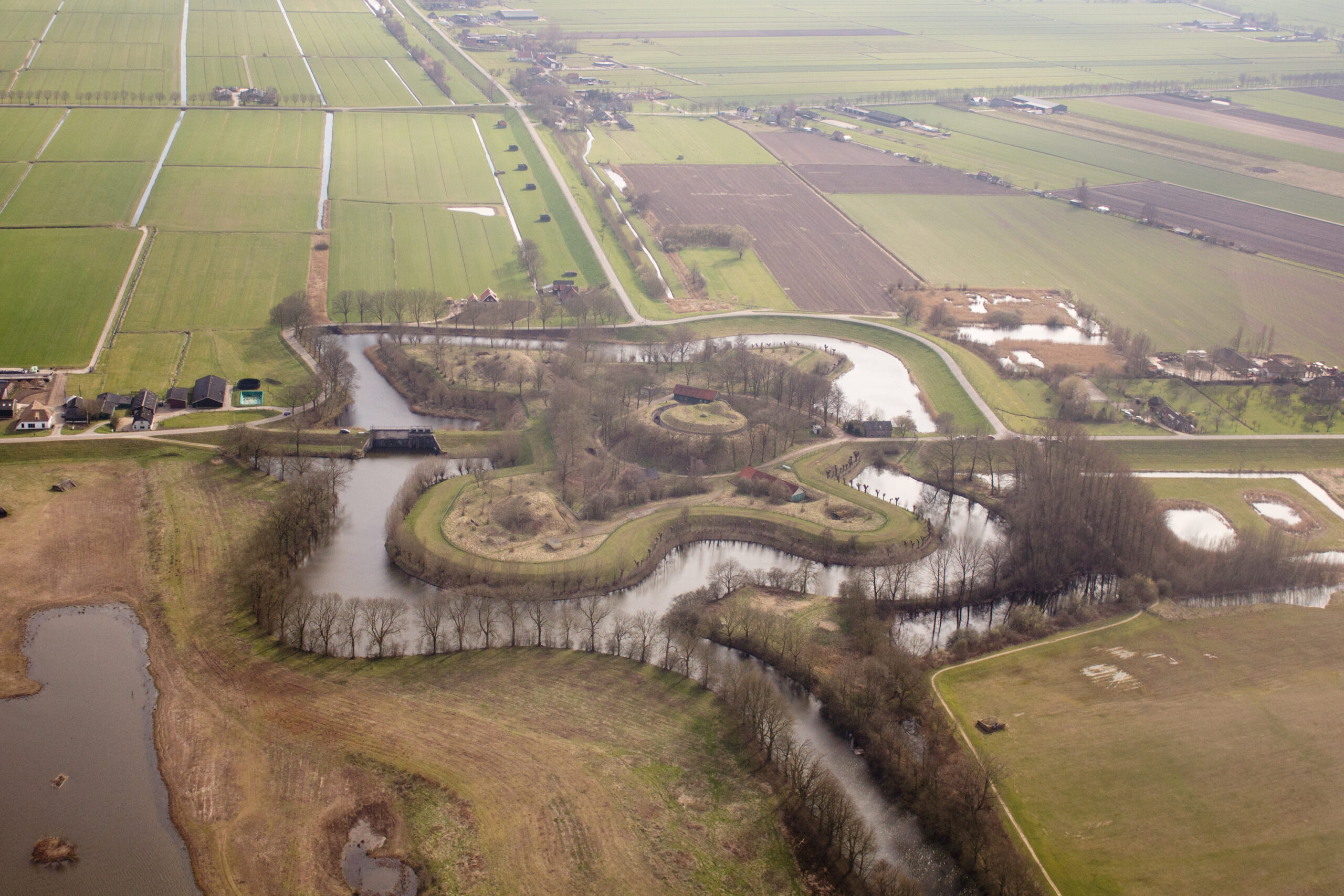 Luchtfoto van een vesting omringd door water en groene velden. Rechte wegen en sloten op de achtergrond.