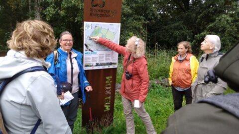 Groep mensen bekijkt samen een kaart bij een informatiebord in Noorderpark Ruigenhoek.
