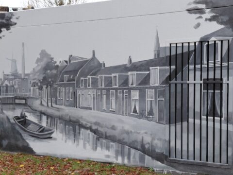 Zwart-wit muurschildering van een Nederlands dorp met grachten, huizen en een molen.