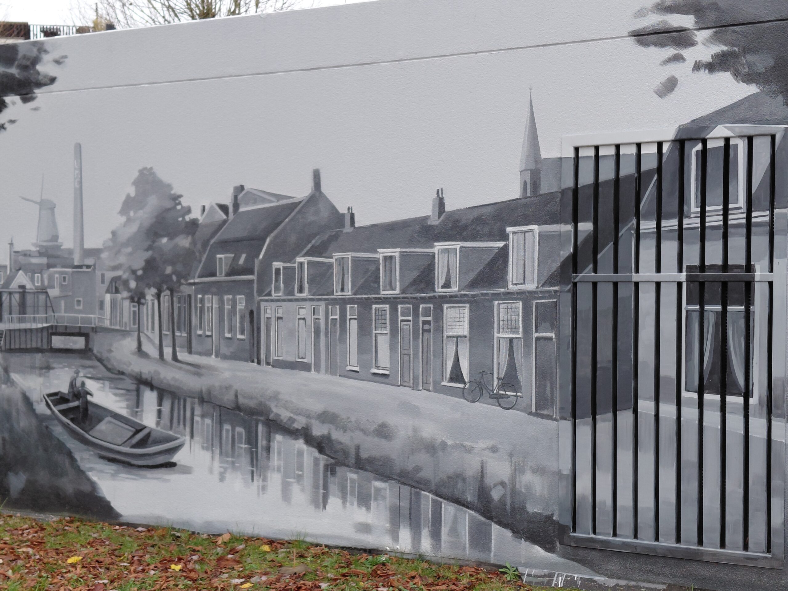 Zwart-wit muurschildering van een Nederlands dorp met grachten, huizen en een molen.