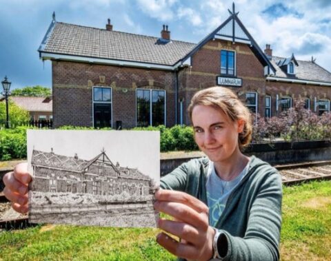 Vrouw houdt tekening van hetzelfde stationsgebouw vast; gebouw op achtergrond.