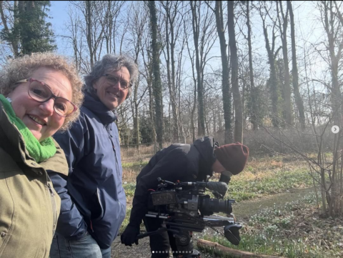 Drie mensen in een bos, een filmt met een camera.