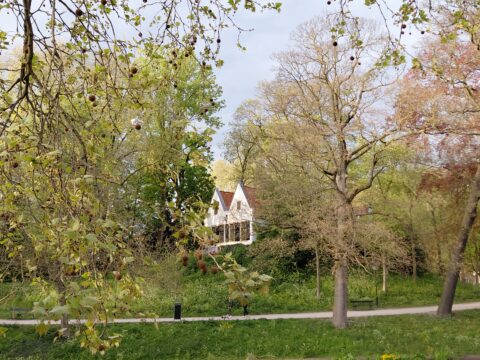 Wit huis omringd door bomen en een wandelpad in een groene parkachtige omgeving.