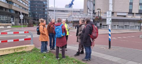 Groep mensen met rugzakken op een straat in een stedelijke omgeving, met moderne gebouwen.