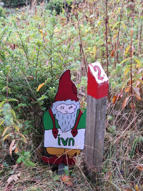 Houten kabouterbord en genummerde paal in een groene omgeving.