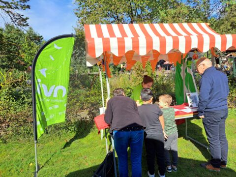 Mensen bij een informatiestand met rood-wit gestreepte luifel, groene vlag met tekst "IVN".