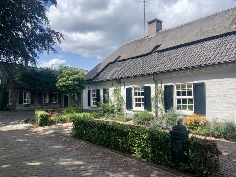 Een traditioneel wit huis met rieten dak en tuin onder wolkenlucht.