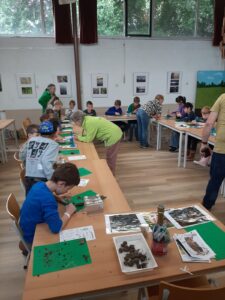 Kinderen in een klas lokalen onderzoeken natuurmaterialen aan tafels met groene onderleggers.