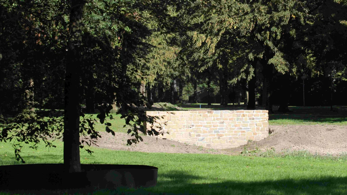 Stenen muur omgeven door bomen in een parklandschap met groene grasvelden.