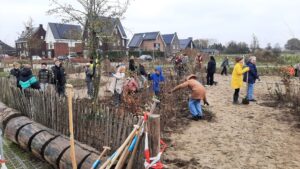 Mensen planten bomen in een gemeenschapstuin; achtergrond met huizen en wolkenlucht.