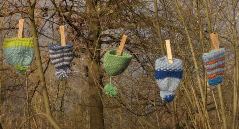 Gebreide mutsen, geklemd aan een waslijn in een bosachtige omgeving.