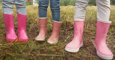 Drie paar benen in regenlaarzen op een modderig veld. Twee roze, één lichtroze.