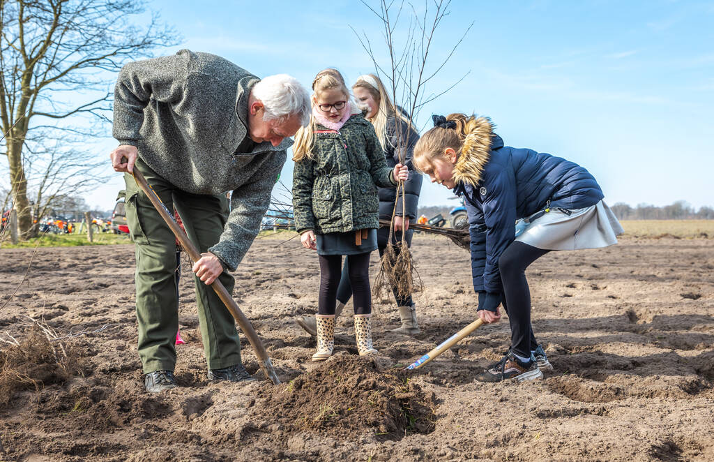 Een man en kinderen planten samen een boom in een veld.