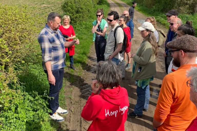 Groep mensen luistert naar een man die uitleg geeft tijdens een wandeling op een landweg.