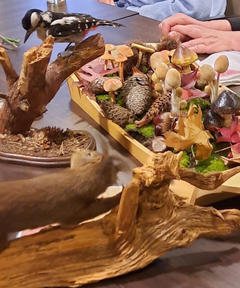 Op tafel een natuurtafereel met houten sculpturen, inclusief een specht en paddenstoelen.
