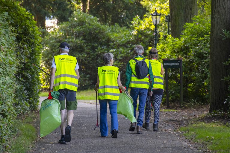 Vier mensen in gele hesjes verzamelen afval in een park, met bord naar 