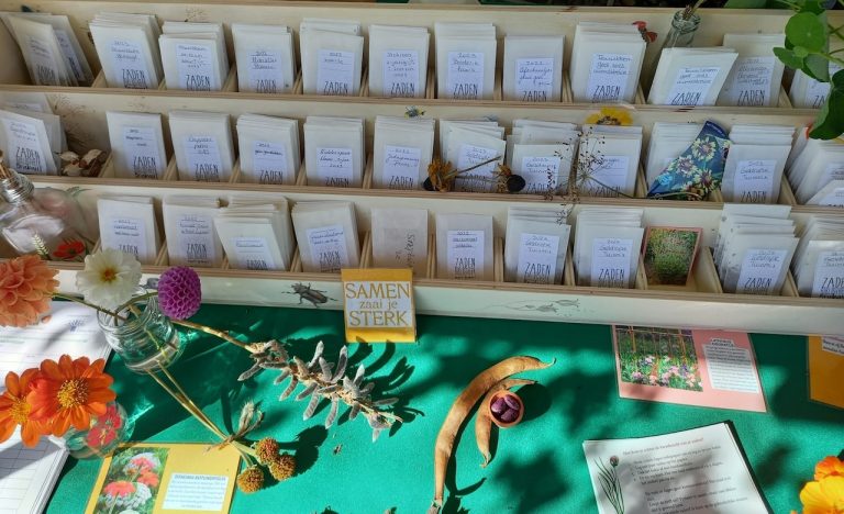 Zaadzakjes en bloemen op een groene tafel met een bordje 