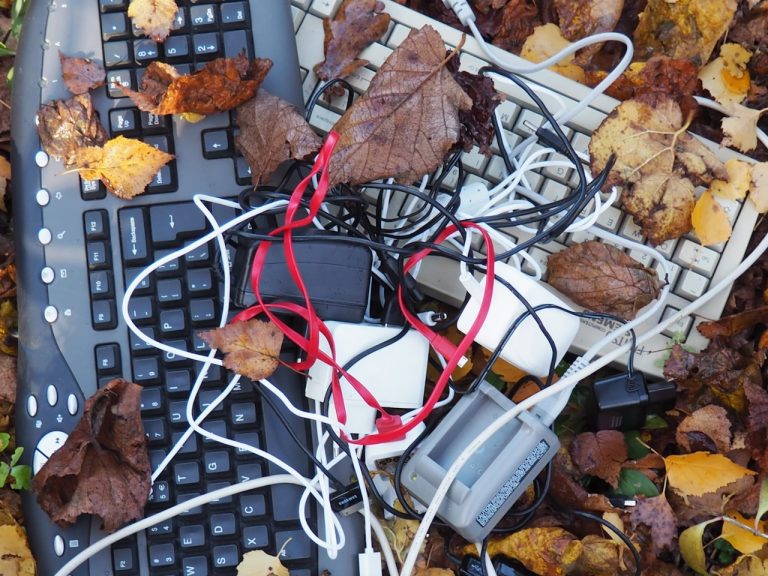 Twee toetsenborden met kabels en bladeren erop, liggend op de grond.