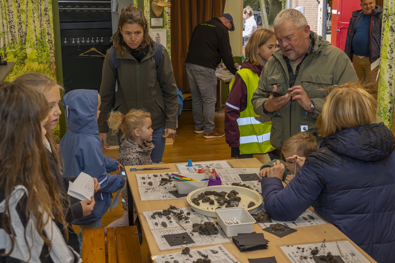 Kinderen en volwassenen onderzoeken materialen op een tafel met dierensporen in een educatief centrum.
