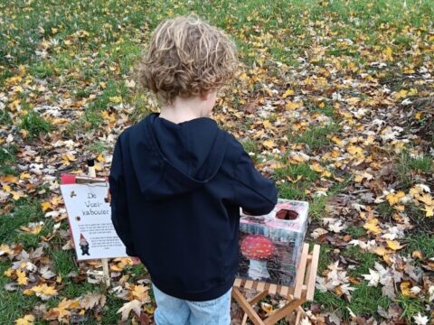 Kind speelt bij herfstbladeren met een voeldoos en een bordje over een kabouter.