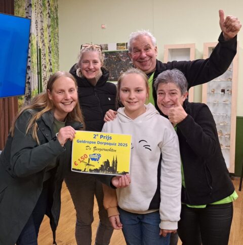 Groep mensen viert het winnen van de tweede prijs in een dorpsquiz, met een cheque van €150.