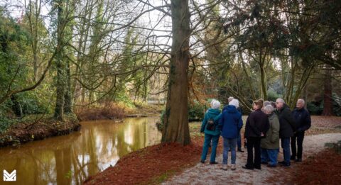 Groep mensen in een bosrijke omgeving kijkt naar een rustige vijver.