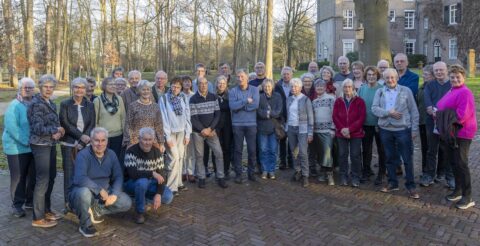 Een groep mensen poseert buiten voor een gebouw, omringd door bomen.