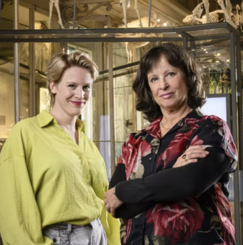 Twee vrouwen poseren in een museum vol vitrines en skeletten.