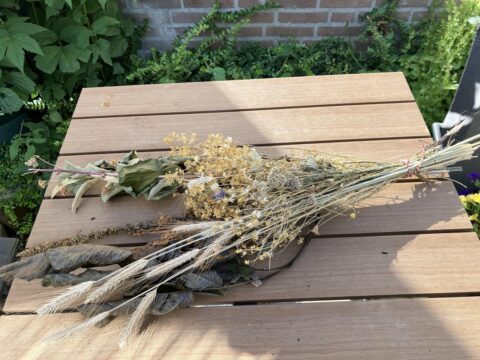 Bos gedroogde bloemen en gras op houten tafel in tuin. Achtergrond vol groene planten.