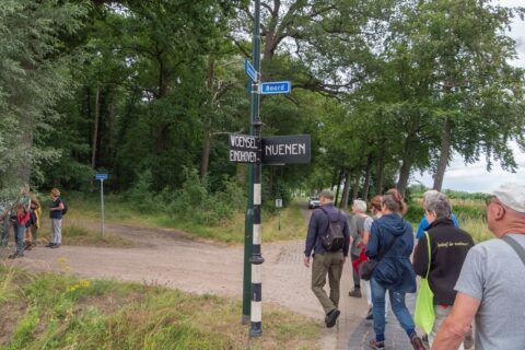 Groep wandelaars op een bospad bij een wegwijzer naar Eindhoven en Nuenen.
