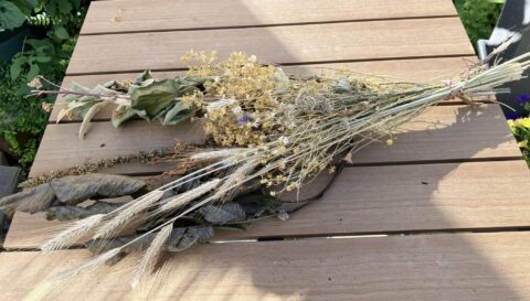 Droogbloemenboeket op houten tafel in zonnige tuin.
