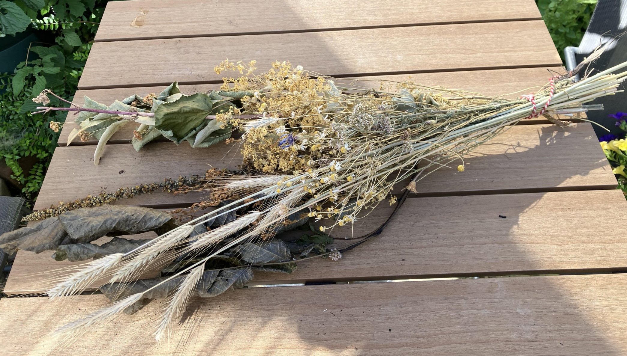 Droogbloemenboeket op houten tafel in zonnige tuin.
