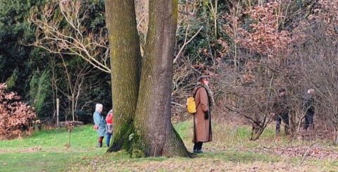 Drie mensen wandelen in een groen park met bomen en struiken in de achtergrond.