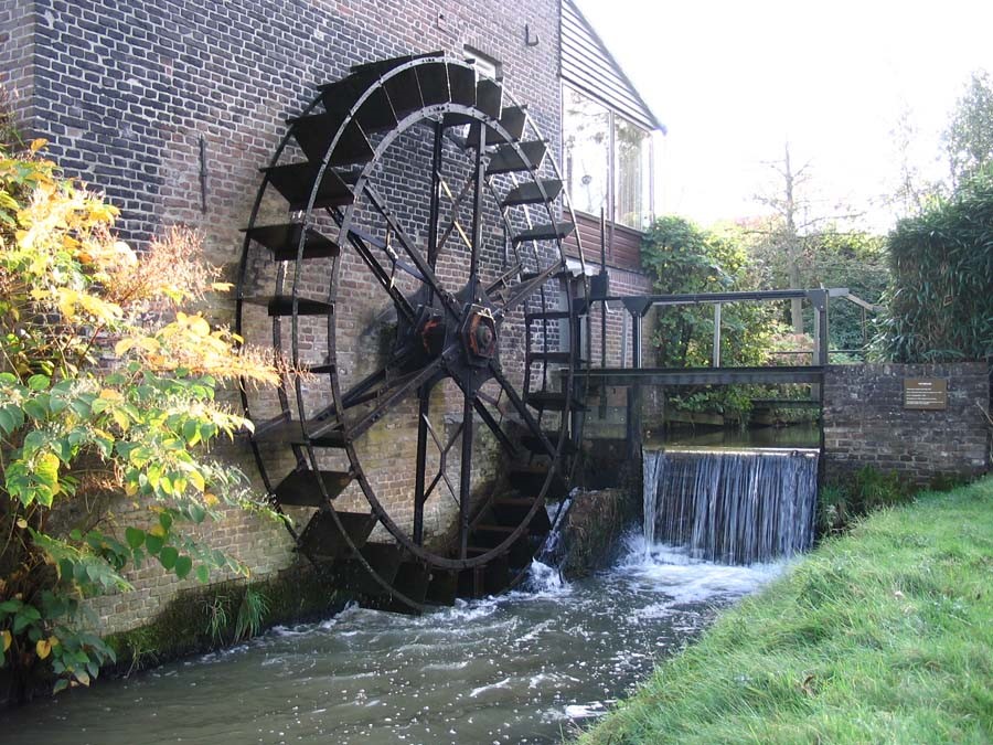 Watermolen bij een bakstenen gebouw met stromend water en groene planten eromheen.
