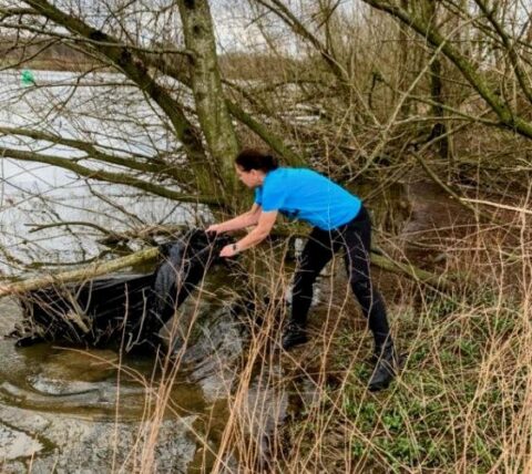 Persoon in blauw shirt verwijdert afval uit een boom bij een rivier.