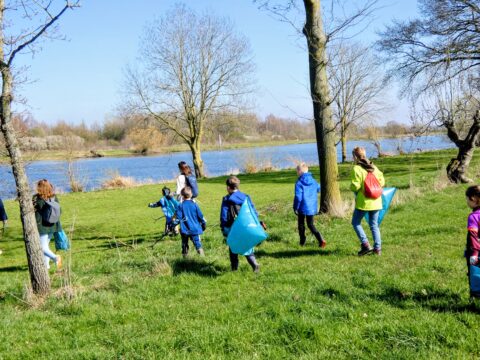 Kinderen met vuilniszakken lopen langs een meer op een zonnige dag om zwerfvuil op te ruimen.