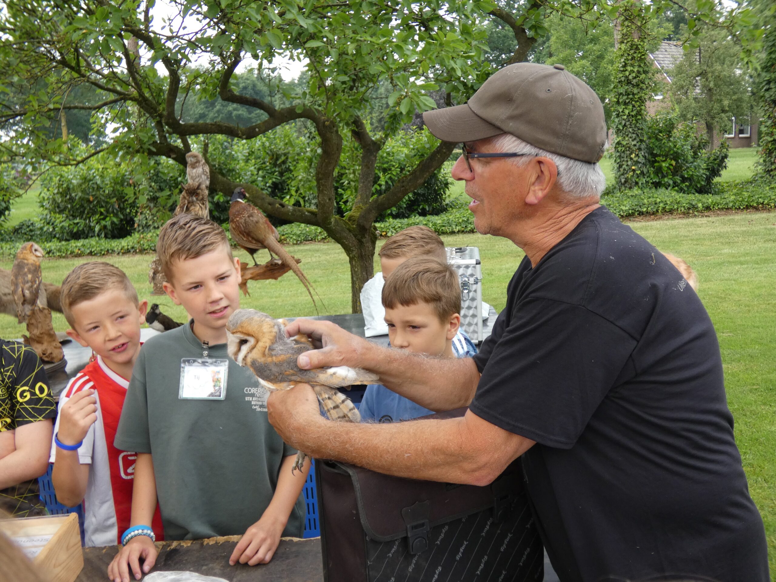 Een man toont een groep kinderen een uil in een parkachtige omgeving.