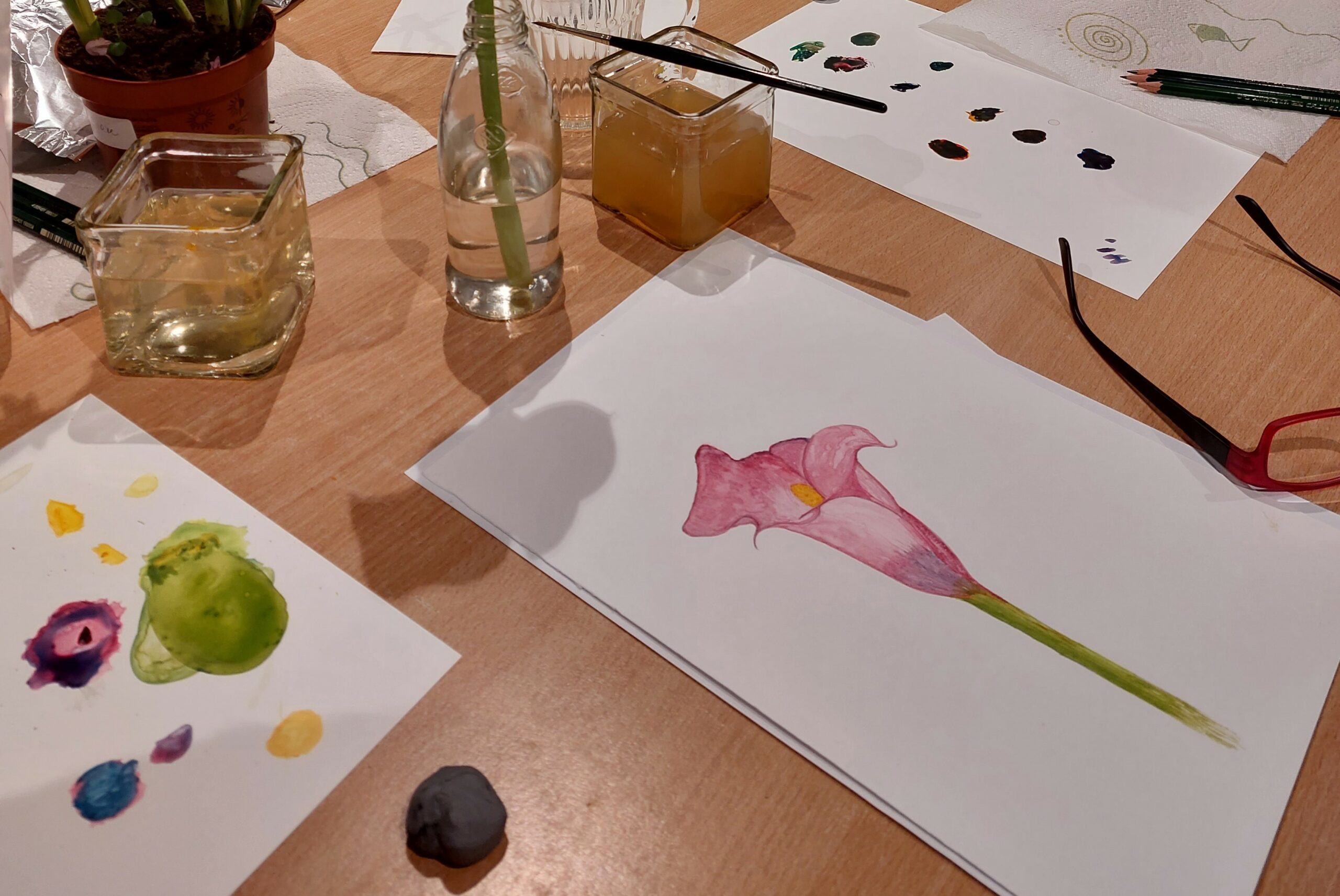 Schilderbenodigdheden en een aquarel van een roze lelie op een tafel.