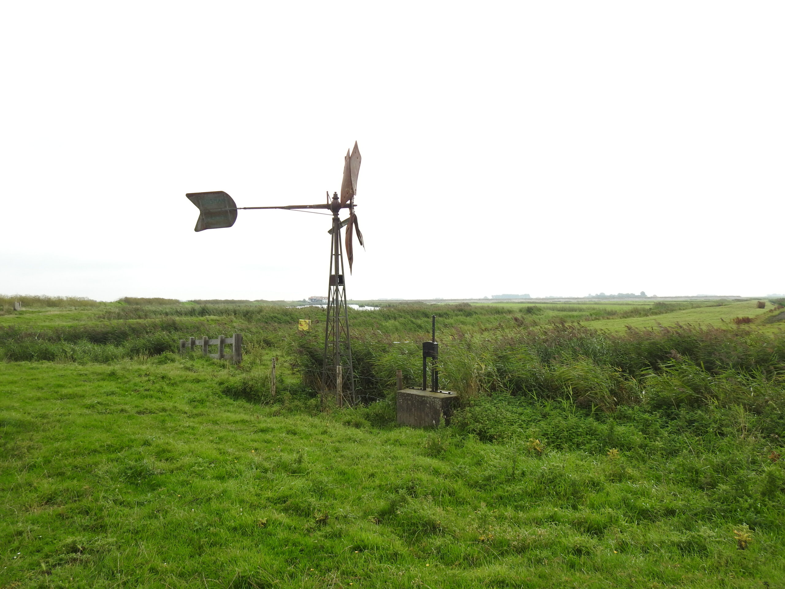 Oude windmolen op grasveld in een weids, groen landschap.