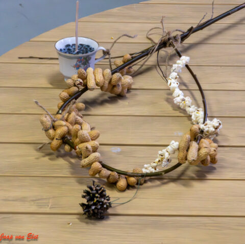 Een krans van pinda’s en popcorn, met een bakje vogelvoer.