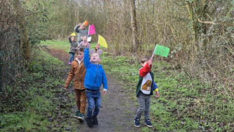 Kinderen lopen op een bospad en zwaaien met kleurrijke vlaggetjes tijdens een buitenspel.