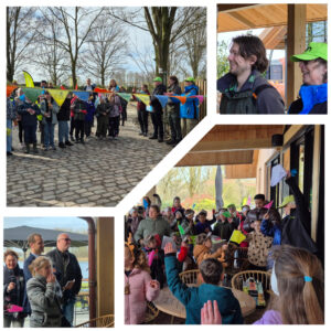 Groep mensen bij buitenbijeenkomst; kinderen zwaaien met vlaggen en volwassenen juichen.