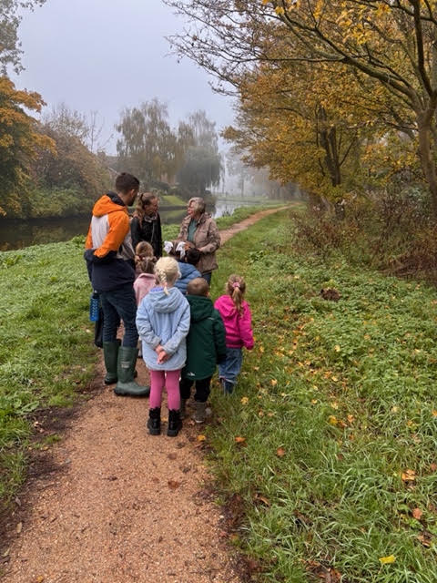 Groep mensen op bosachtig pad in de herfst, omgeven door bomen en nevel.