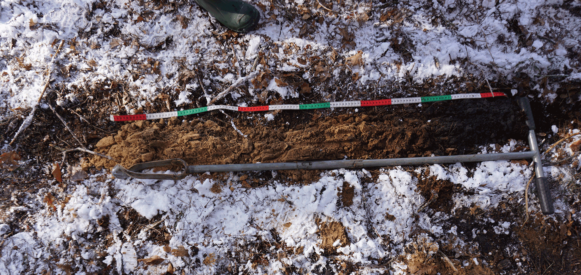 Bodemmonster in sneeuw, gemeten met gekleurde liniaal, naast een boortoestel.