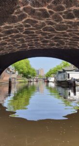 Kanaal onder een bakstenen brug met bomen en gebouwen op de achtergrond.